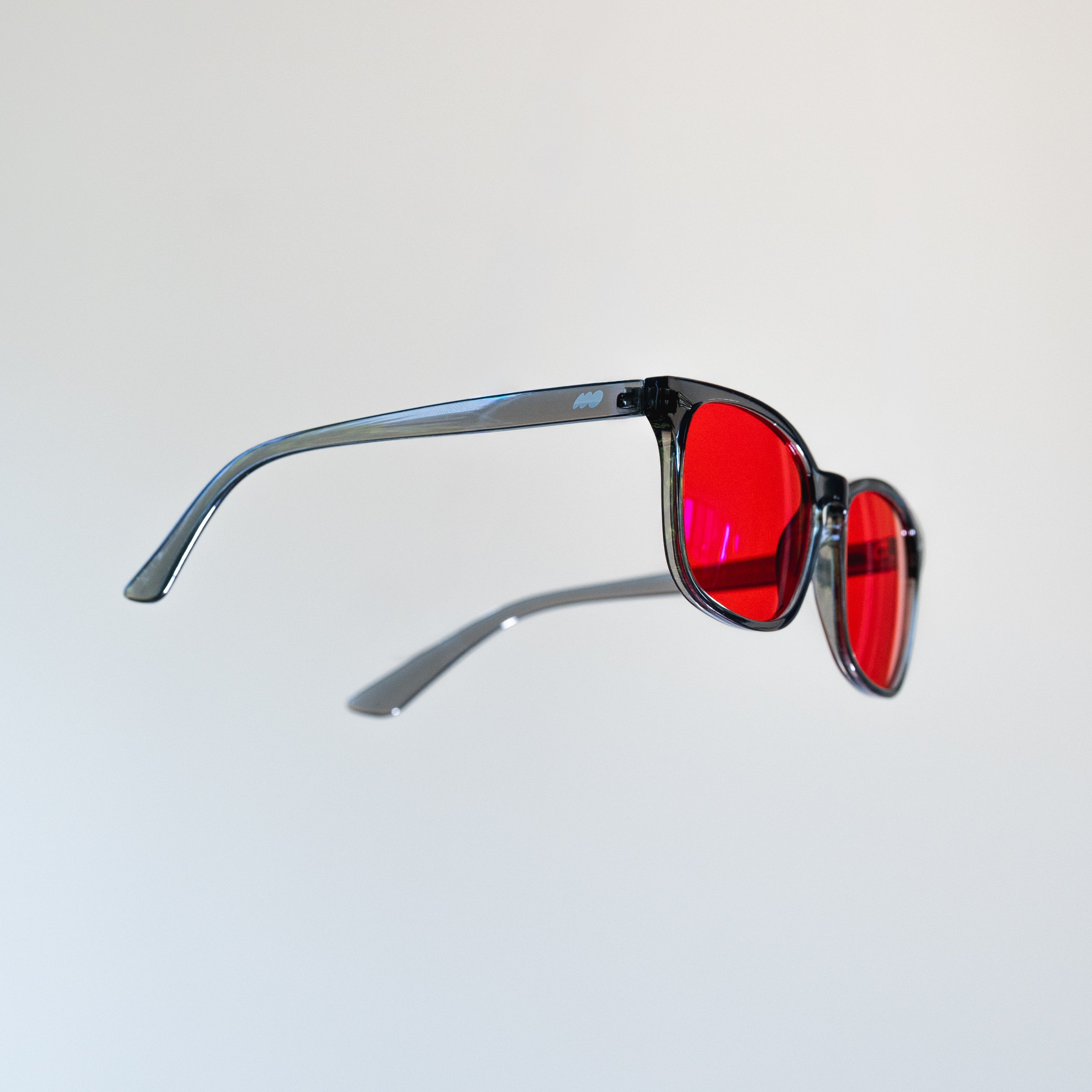 A pair of sunglasses with a translucent dark gray frame and vibrant red lenses, shown floating against a plain light gray background.