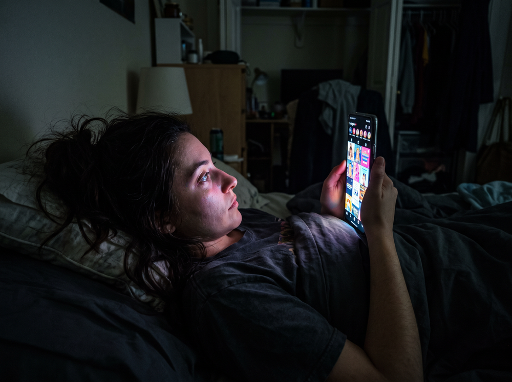 Someone scrolling a bright phone in bed late at night
