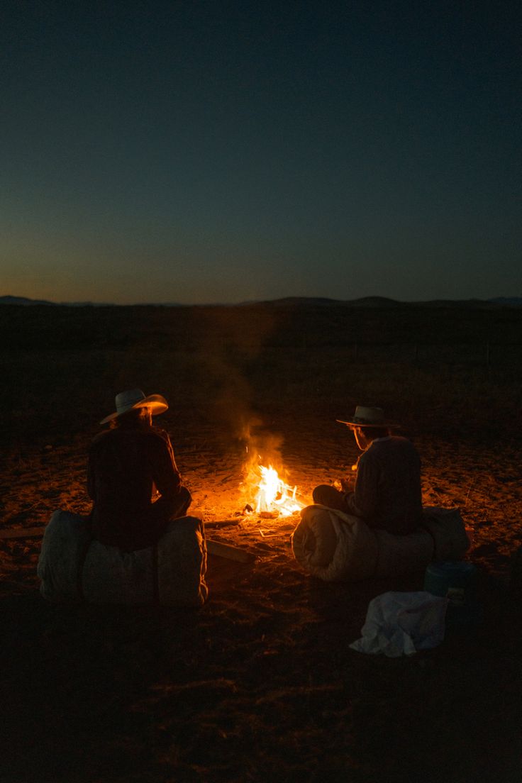 Two people sitting by a campfire at dusk