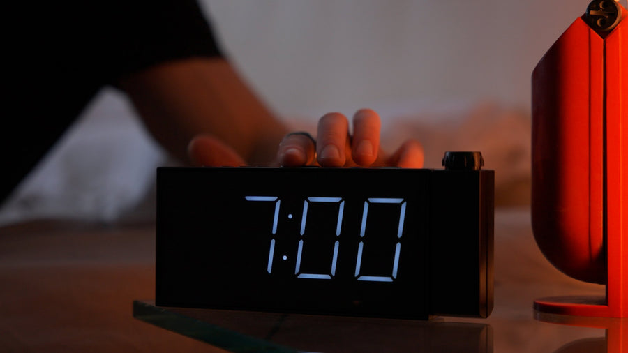 Hand reaching for an alarm clock showing 7:00