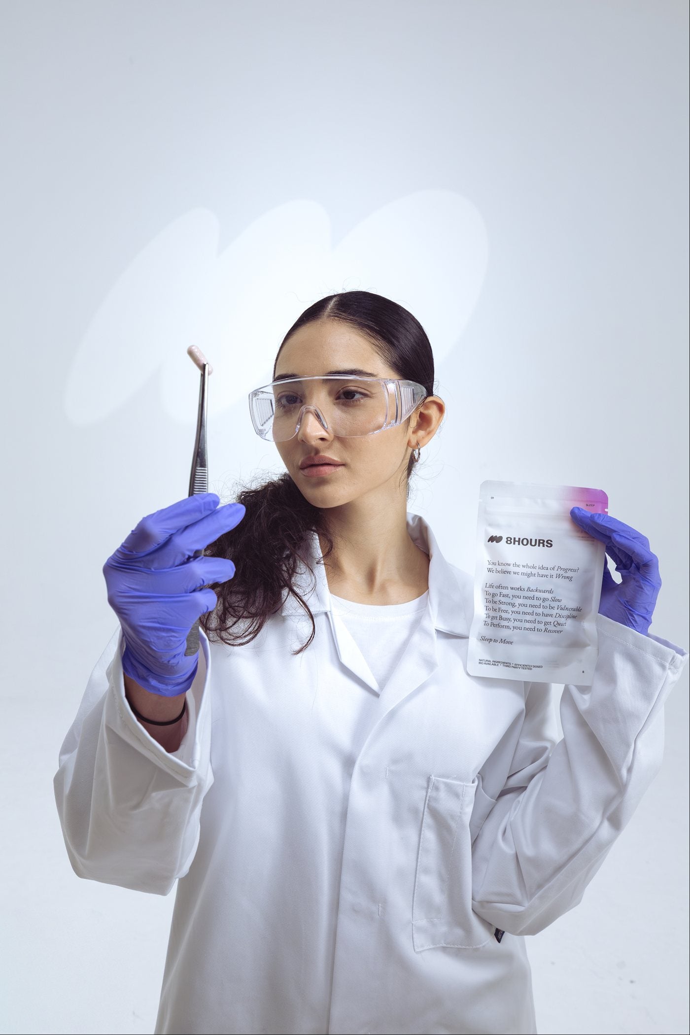 Scientist in safety glasses holding an 8HOURS sachet and tweezers